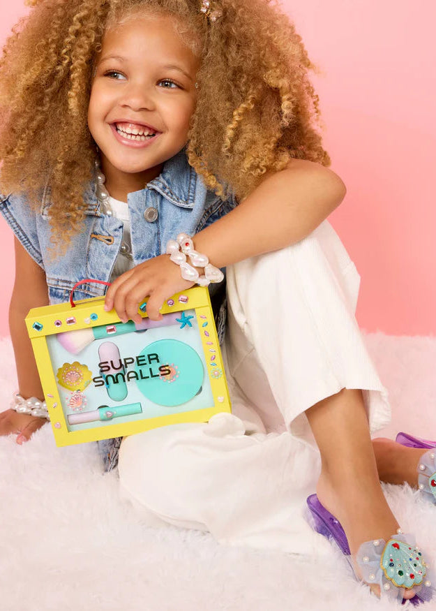 Child holding a toy with 'Super Smalls' branding against a pink background