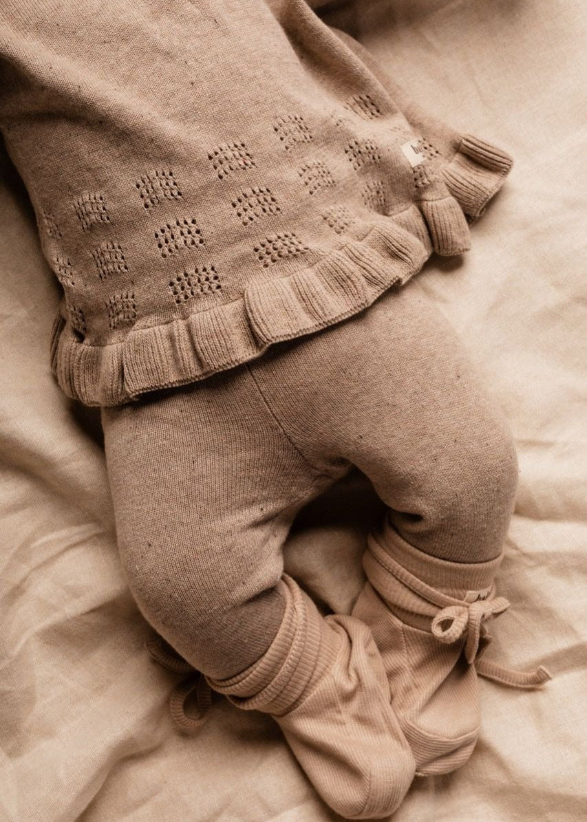 Sepia-toned image of a child's legs wearing a patterned sweater and pants on a soft surface.