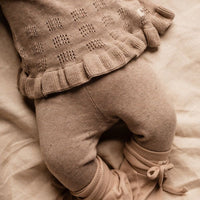Sepia-toned image of a child's legs wearing a patterned sweater and pants on a soft surface.