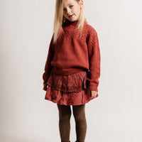 Young girl wearing a red sweater and skirt with brown tights and shoes on a white background