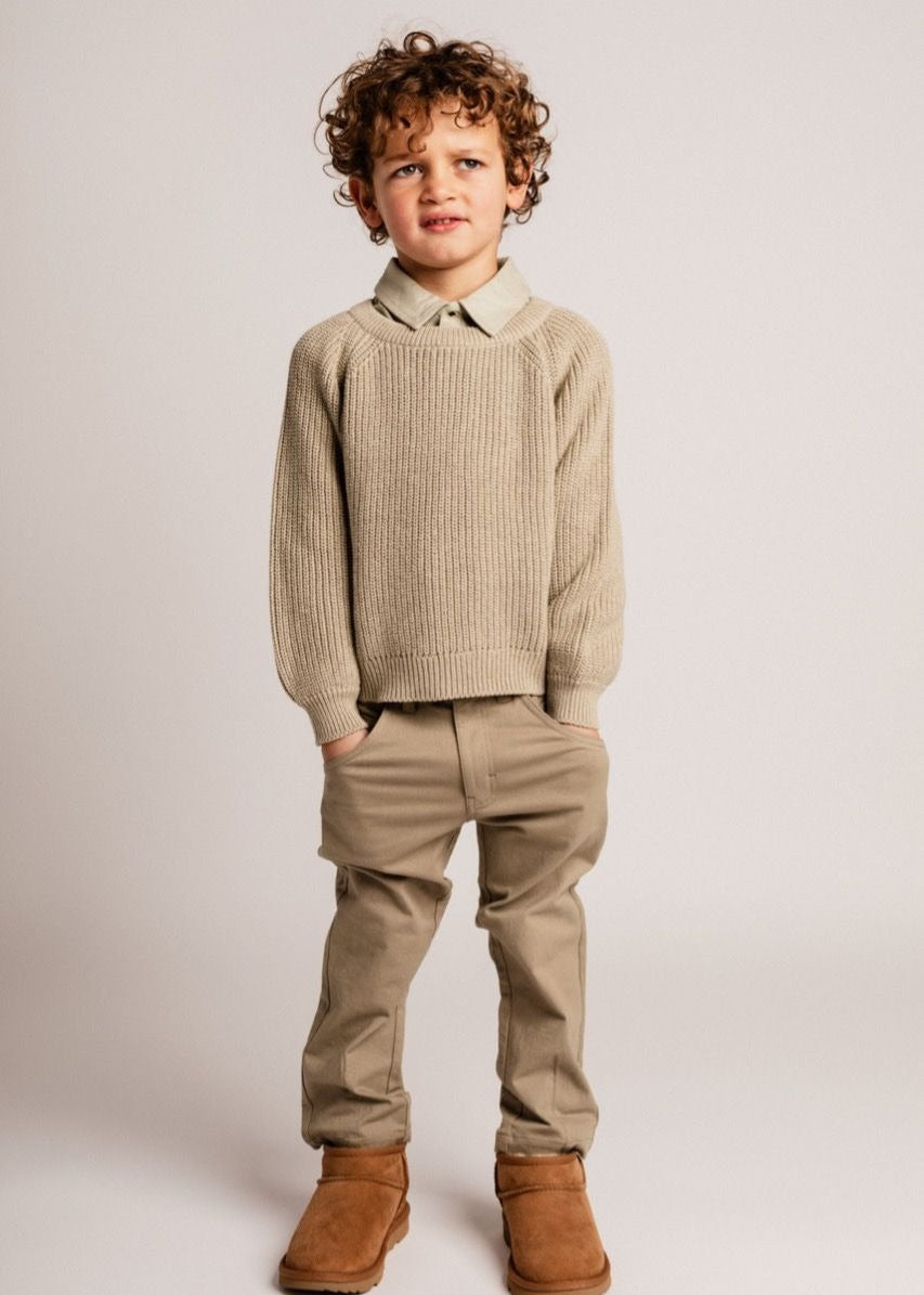 Child wearing a beige sweater, pants, and boots on a plain background