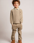 Child wearing a beige sweater, pants, and boots on a plain background