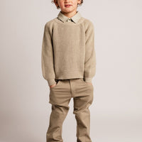 Child wearing a beige sweater, pants, and boots on a plain background