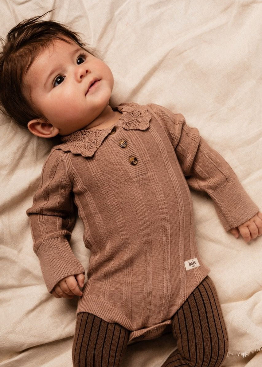 Baby wearing a brown ribbed outfit with a collar, lying on a soft surface.