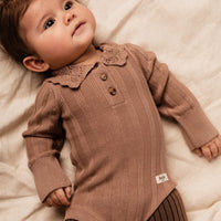Baby wearing a brown ribbed outfit with a collar, lying on a soft surface.