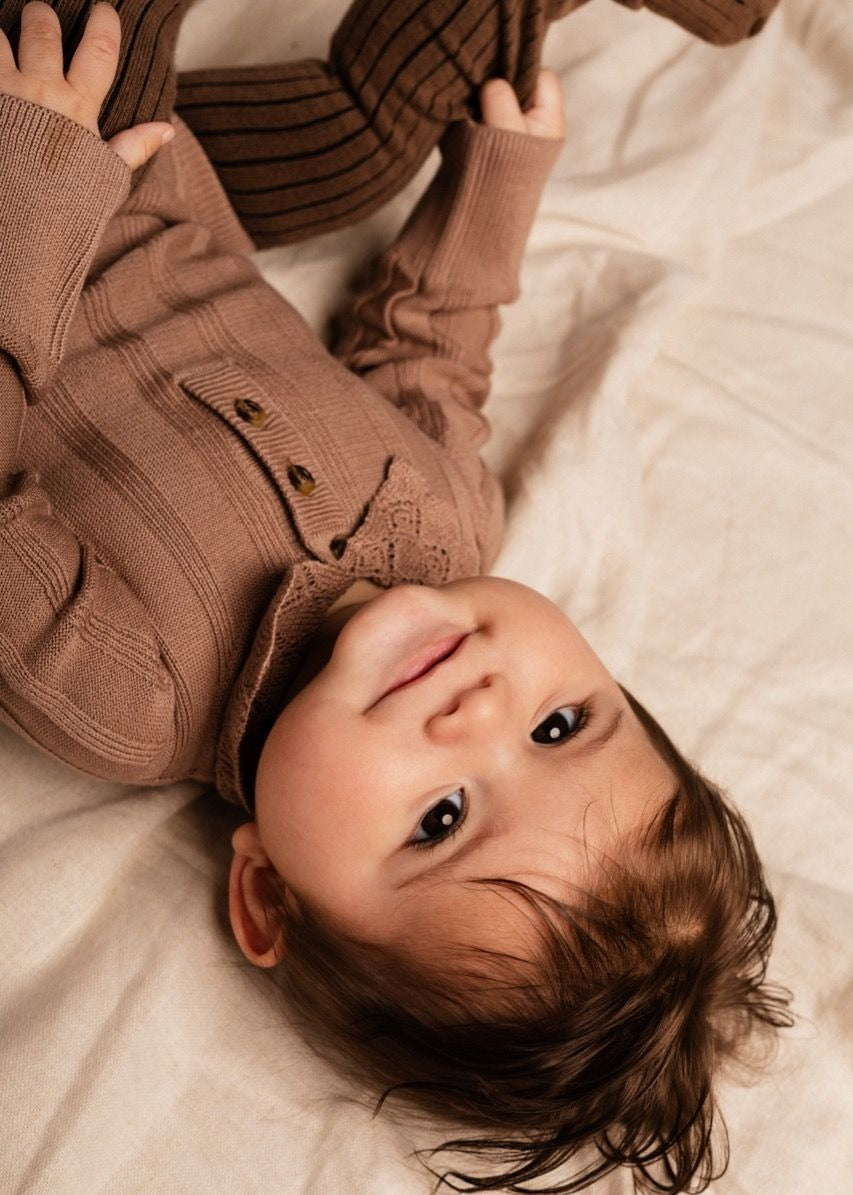 Baby wearing a brown sweater lying on a soft surface