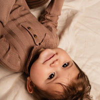 Baby wearing a brown sweater lying on a soft surface