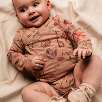 Baby wearing a floral onesie lying on a soft surface