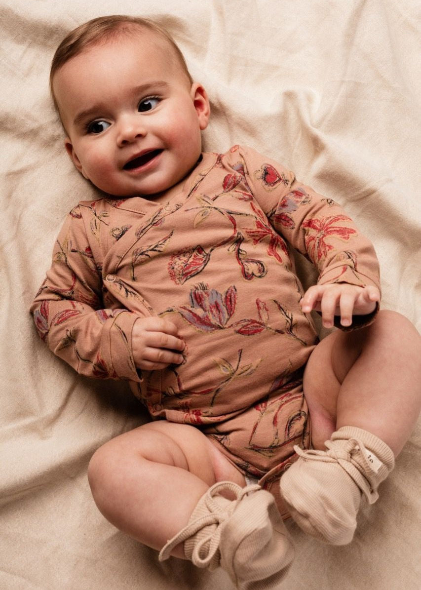 Baby wearing a floral onesie lying on a soft surface
