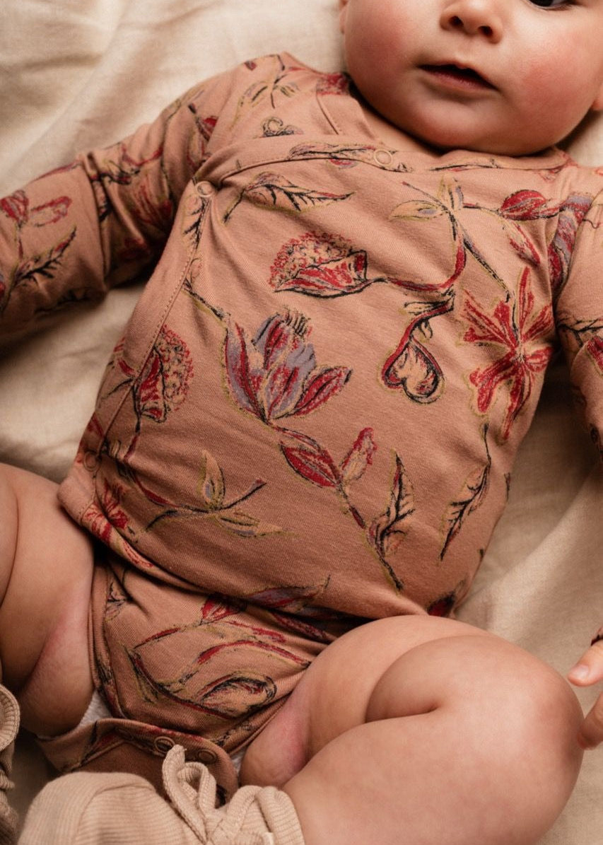 Baby wearing a floral-patterned outfit on a soft surface