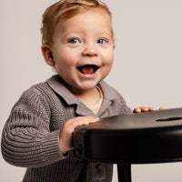 Child in a gray sweater holding a black object against a plain background