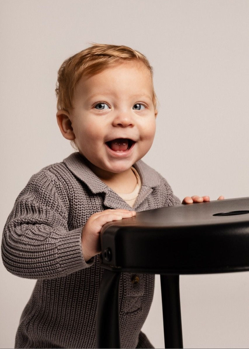 Child in a gray sweater holding a black object against a plain background