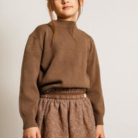 Child wearing a brown sweater and skirt against a plain background