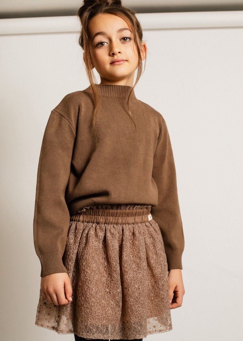 Child wearing a brown sweater and skirt against a plain background