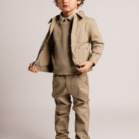 Child wearing a beige coat, sweater, pants, and boots on a plain background