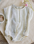 Baby romper on a textured surface with flowers and a bowl in the background
