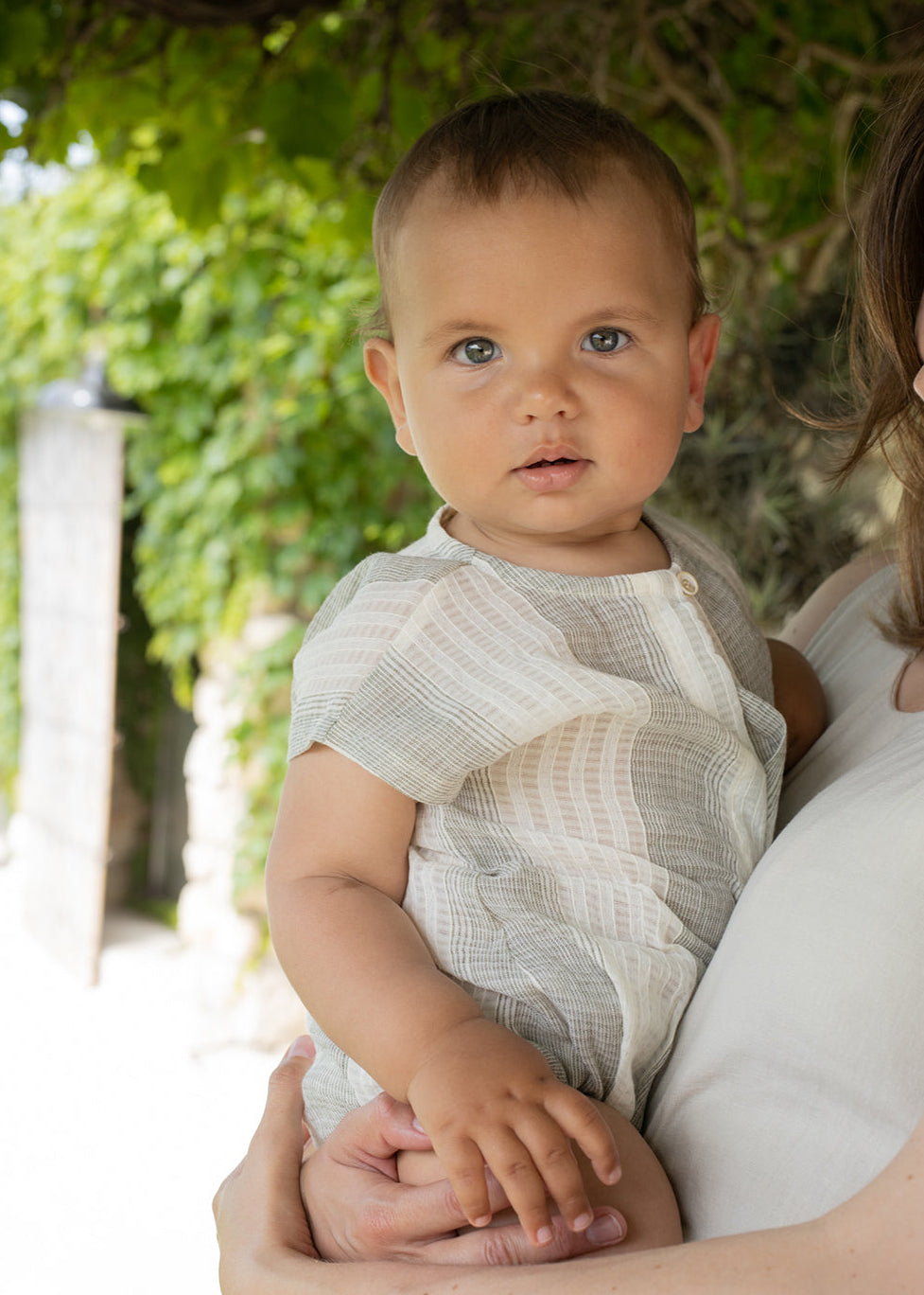 Baby being held by a person with greenery in the background