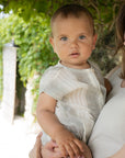 Baby being held by a person with greenery in the background
