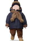 Doll wearing a navy coat, brown pants, and hat with a scarf on a white background