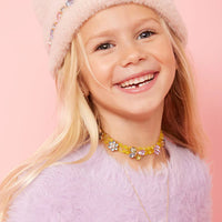 Young girl wearing a pink fluffy hat and colorful necklace against a pink background