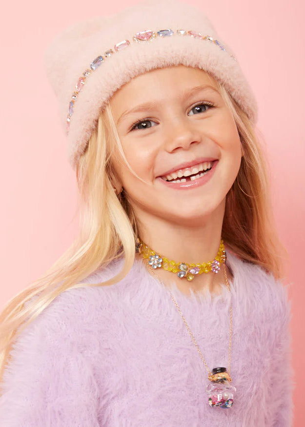 Young girl wearing a pink fluffy hat and colorful necklace against a pink background