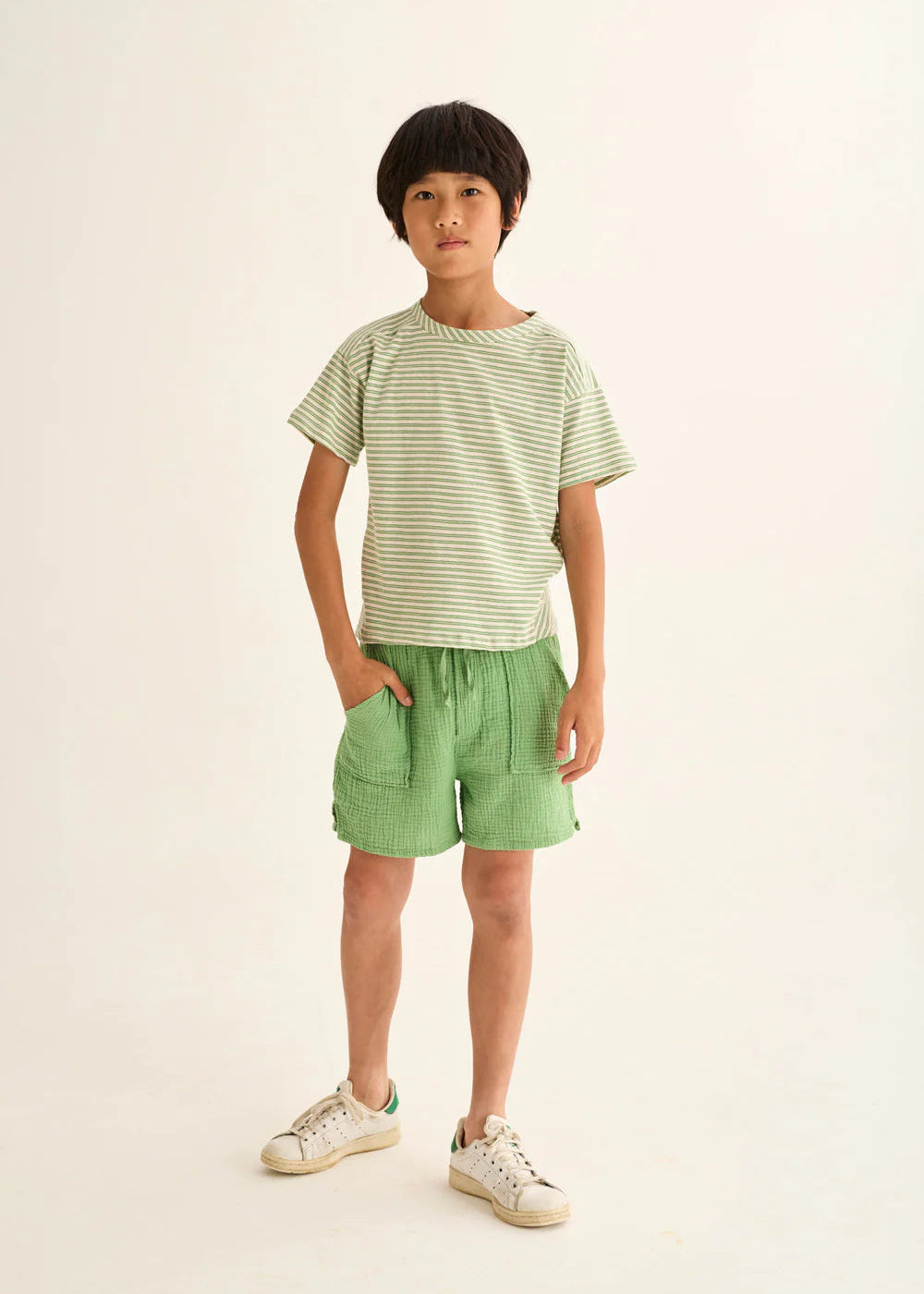 Child wearing a striped shirt and green shorts on a plain background