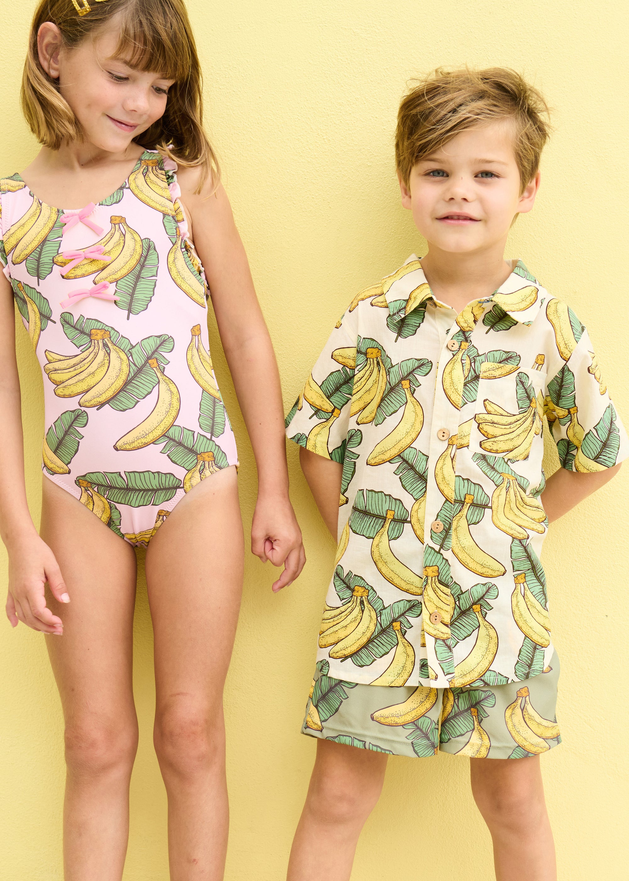 Two children wearing banana-themed clothing on a yellow background