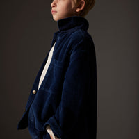 Young boy wearing a dark blue corduroy jacket against a gray background