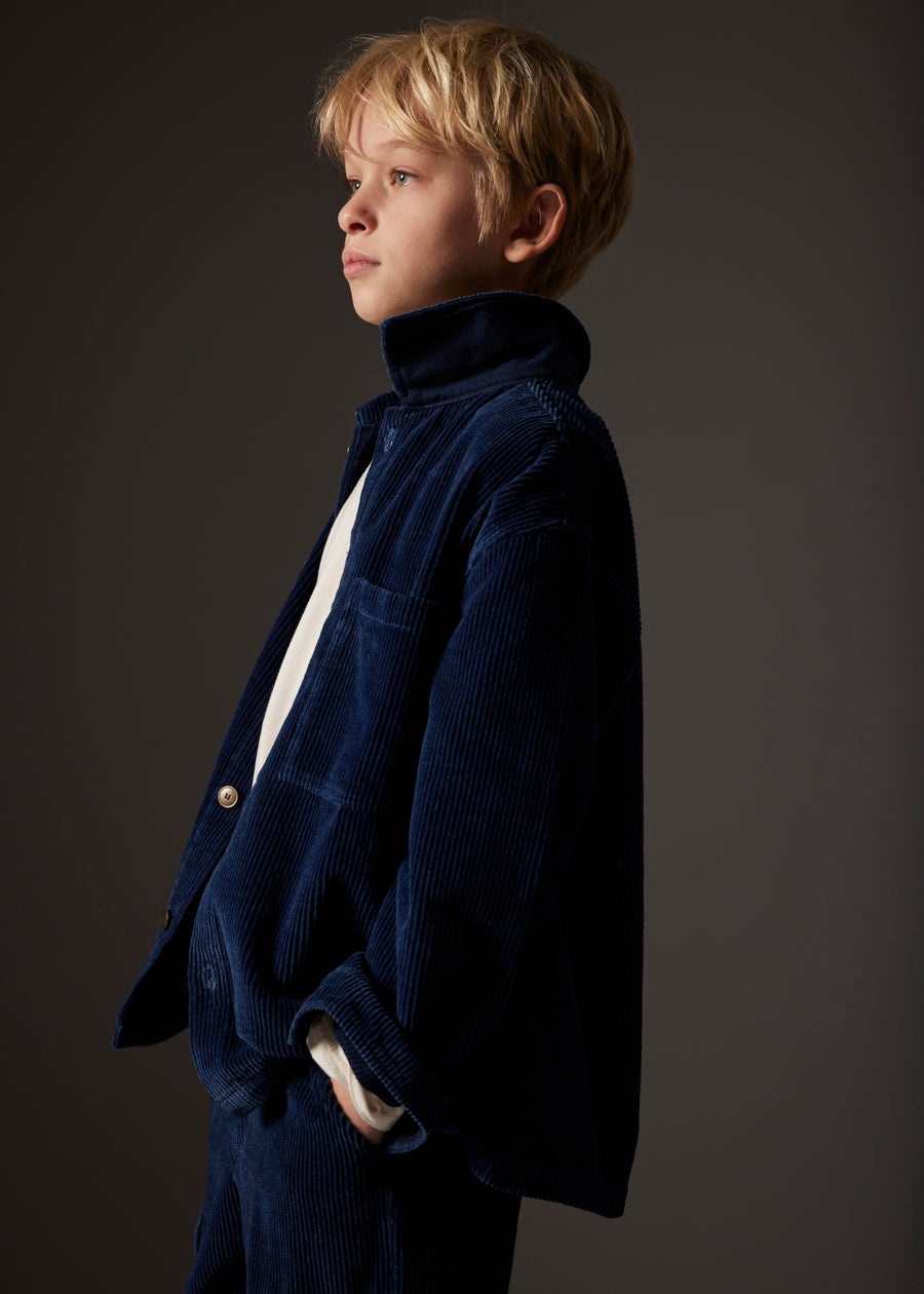 Young boy wearing a dark blue corduroy jacket against a gray background