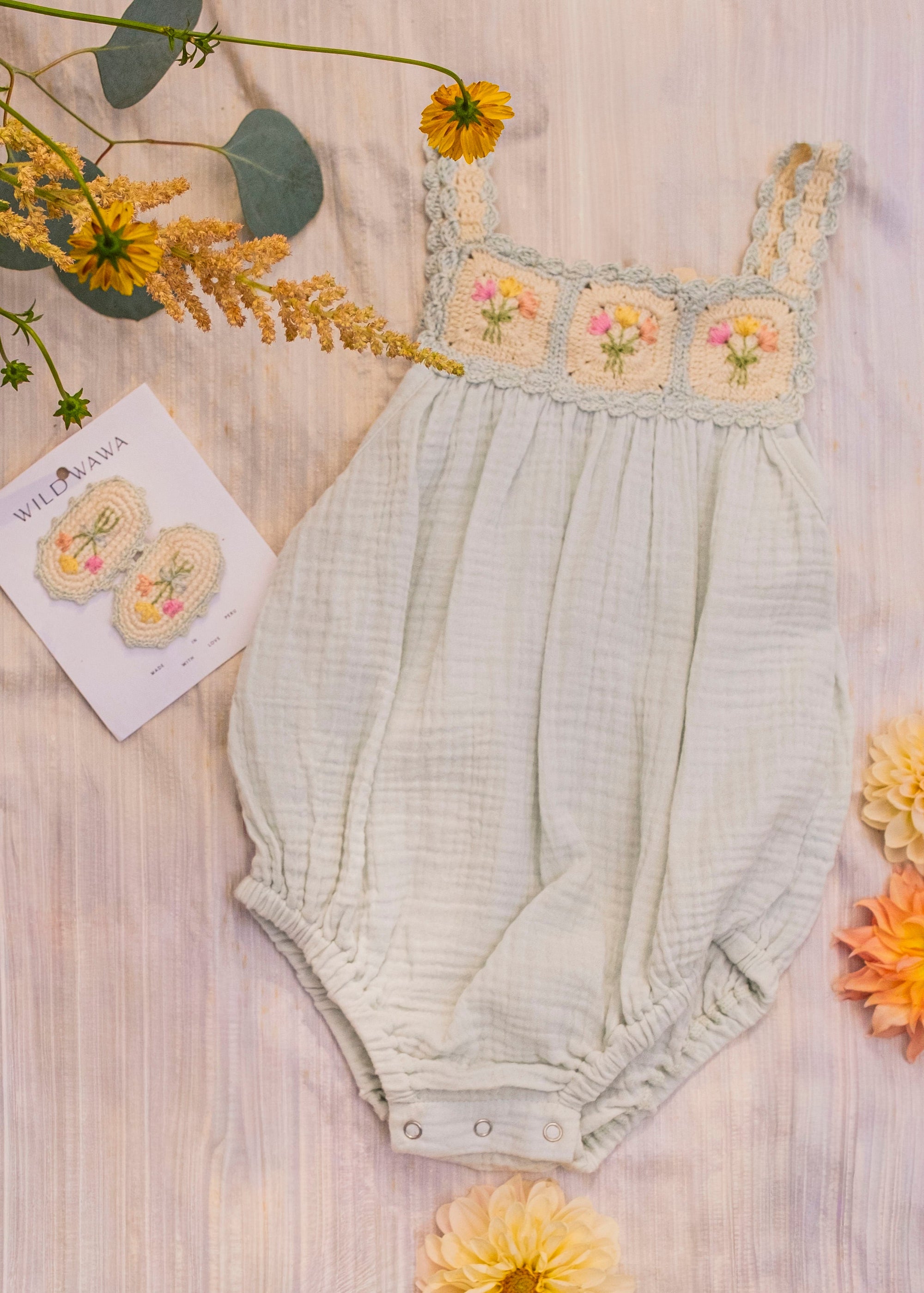 Baby romper with floral embroidery on a wooden surface with flowers around