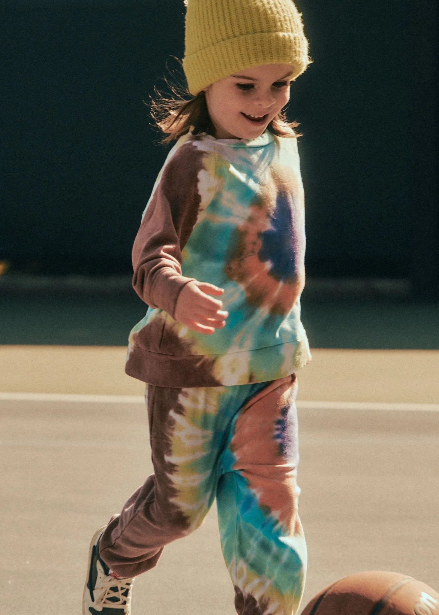 Child wearing a tie-dye outfit and yellow beanie on a basketball court