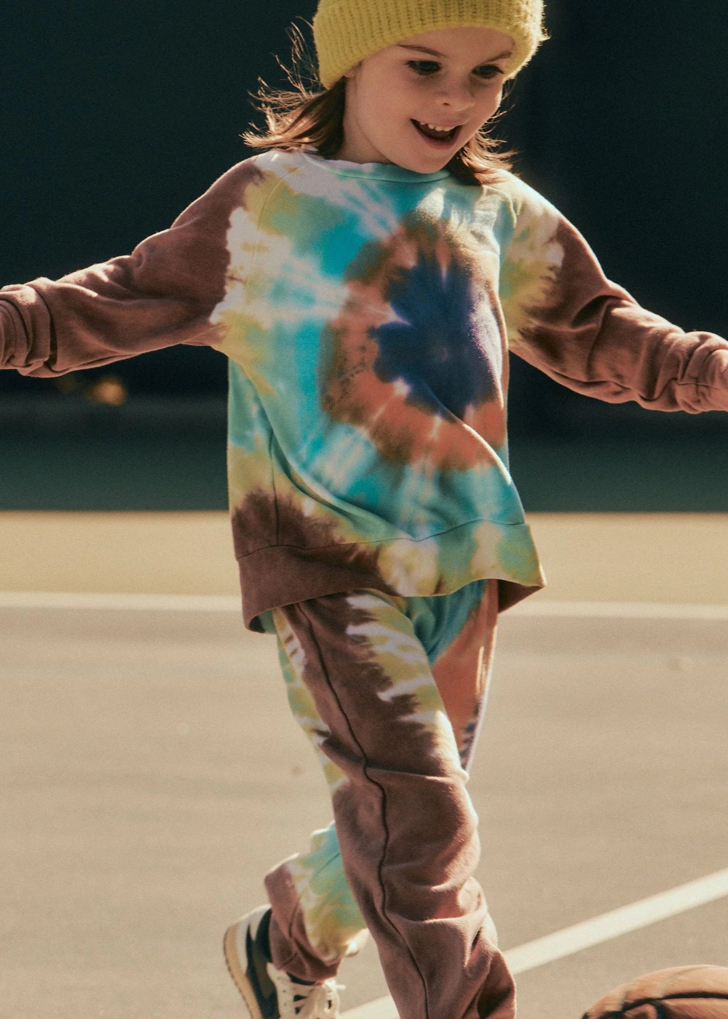 Child wearing a tie-dye shirt and pants on a basketball court