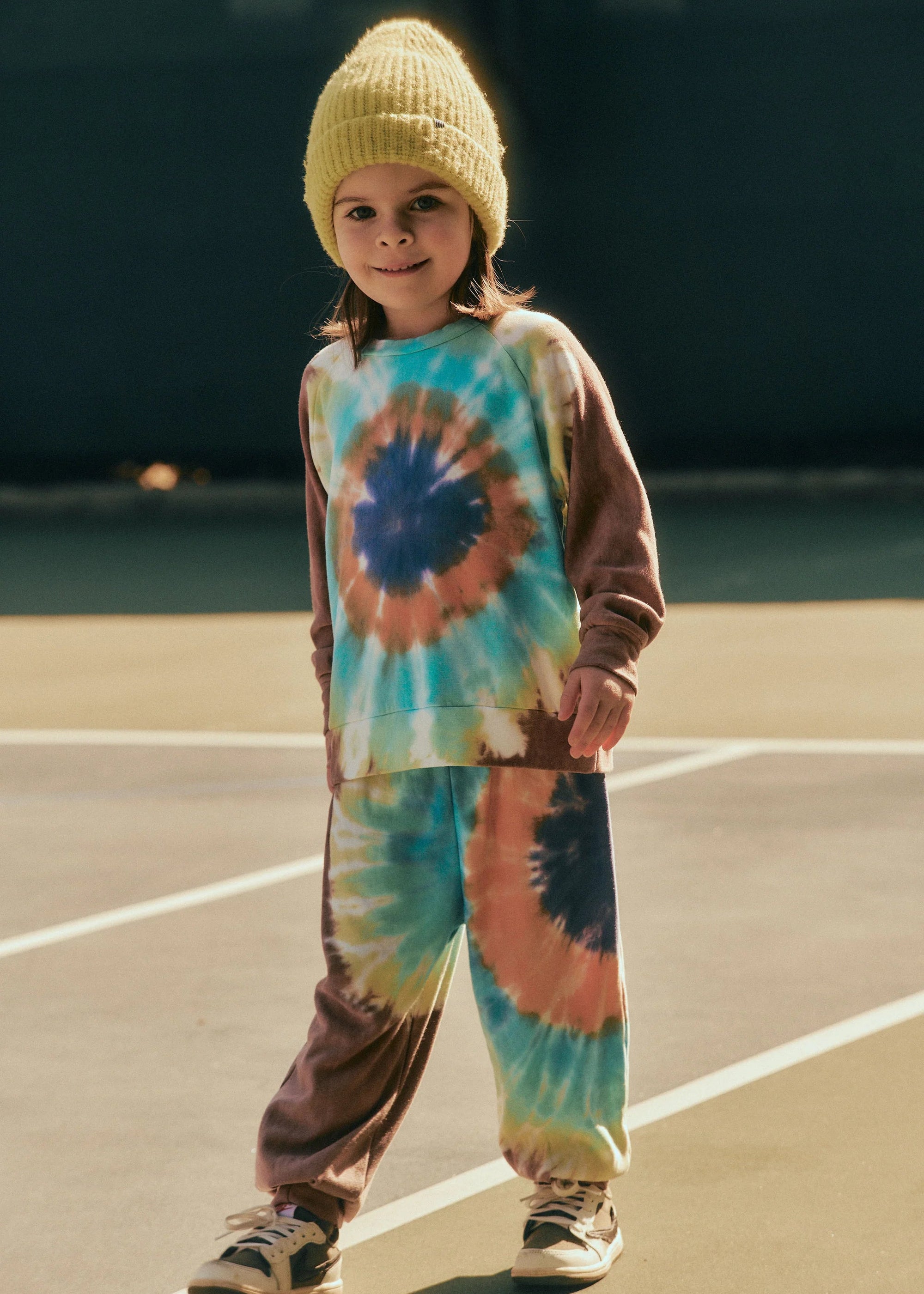 Child wearing a tie-dye outfit with a beanie on a beach.