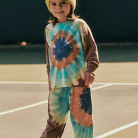 Child wearing a tie-dye outfit with a beanie on a beach.
