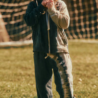 Child standing on grass wearing a dark jacket and light pants with a checkered tent in the background