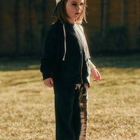 Child wearing a black outfit with a beige cap standing on grass