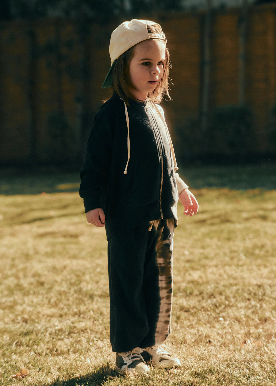 Child wearing a black outfit with a beige cap standing on grass