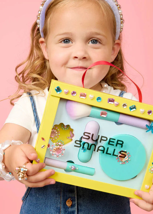 Child holding a 'Super Smalls' product set against a pink background