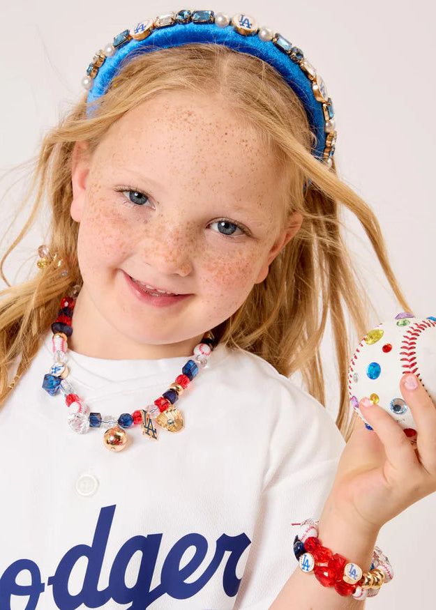 Young girl wearing a Dodgers jersey, headband, and jewelry holding a baseball.