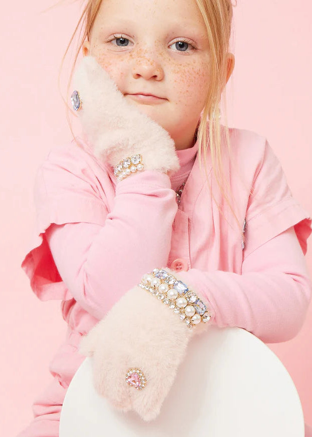 Child wearing pink coat and embellished gloves against a pink background
