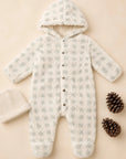 A baby one-piece hooded sleeper in a soft textured fabric with a light gray and cream check pattern, laid flat on a beige background alongside a cream knit beanie and two pinecones.