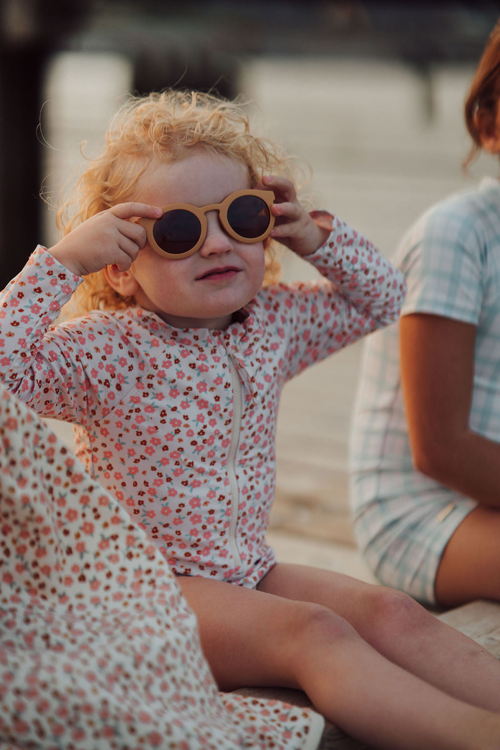 Child wearing sunglasses and a floral swimsuit sitting outdoors