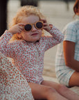 Child wearing sunglasses and a floral swimsuit sitting outdoors