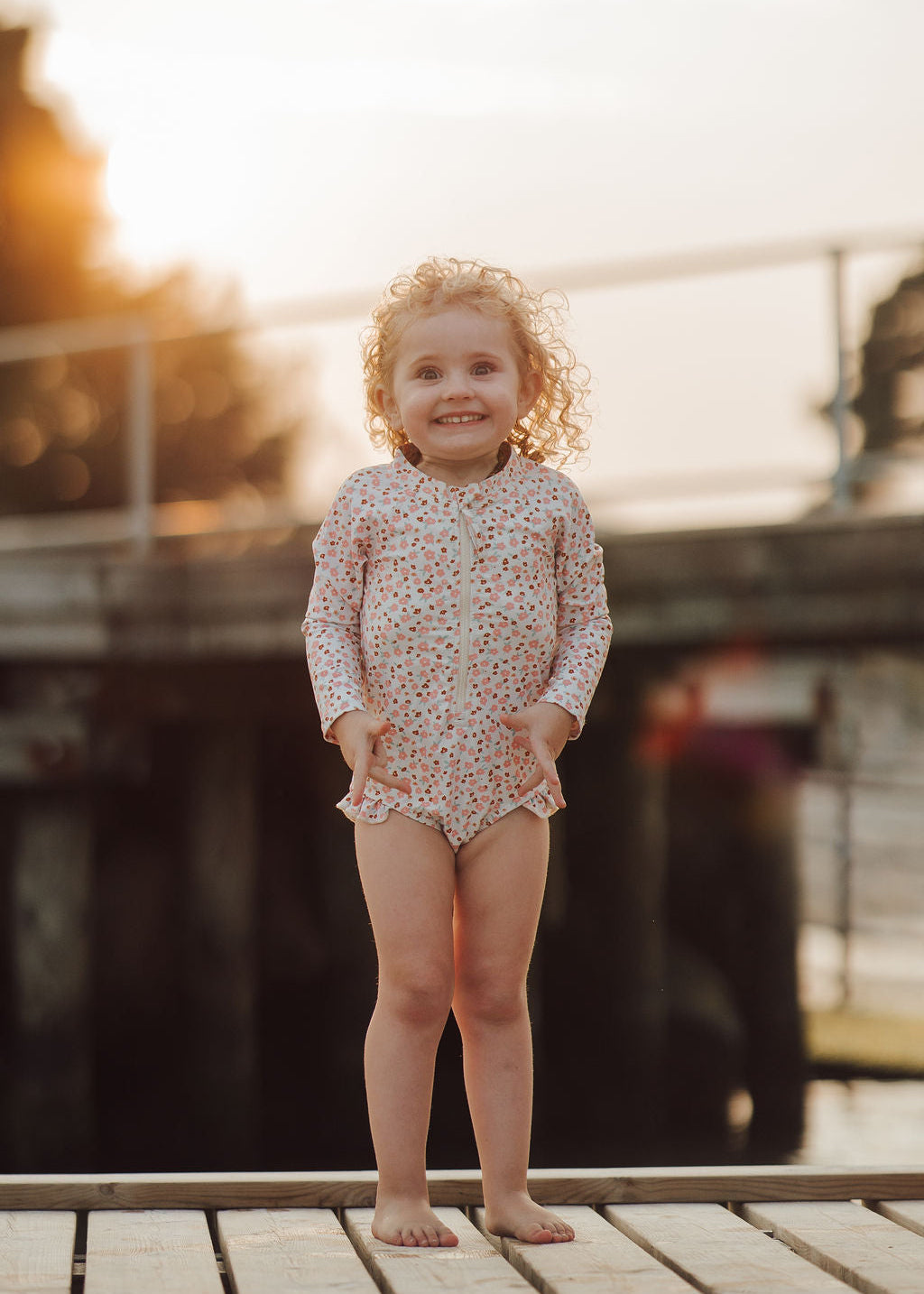 Child in a floral swimsuit standing on a dock with a blurred background