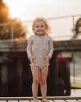 Child in a floral swimsuit standing on a dock with a blurred background