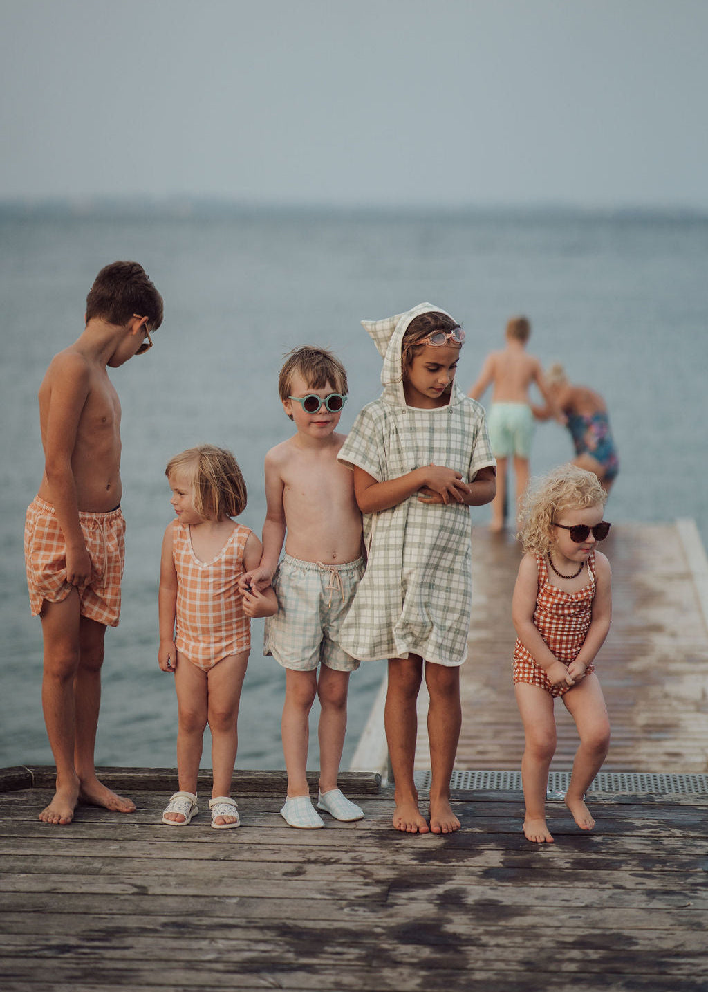 Children on a wooden dock by the water, wearing matching outfits.