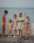 Children on a wooden dock by the water, wearing matching outfits.
