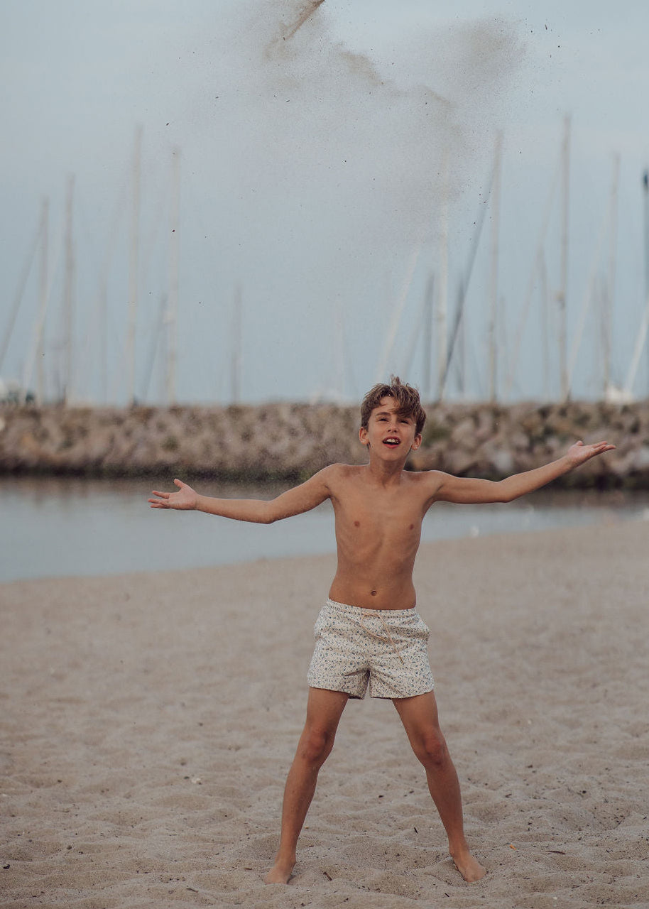Young boy standing on a beach with sailboats in the background