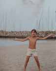 Young boy standing on a beach with sailboats in the background