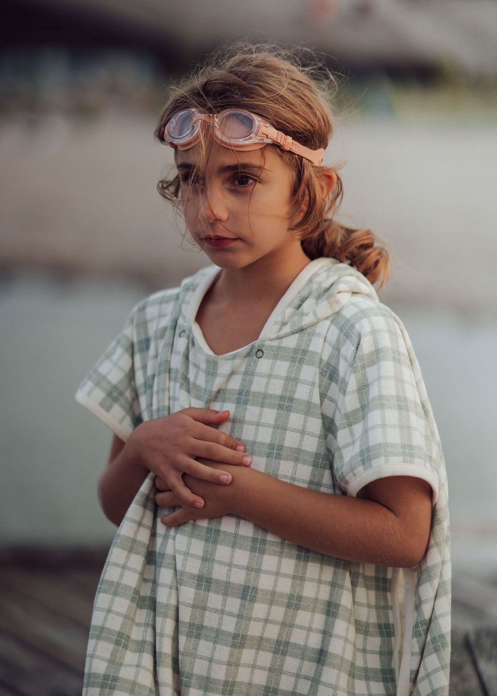 Young girl wearing goggles and a checkered dress by a body of water